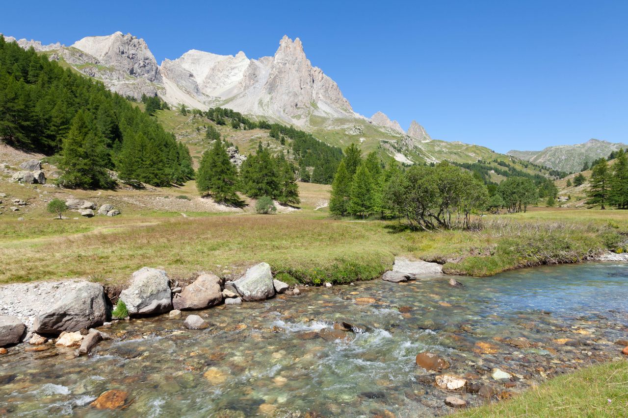 Stunning view of mountains and clear river in Briançon, France with lush greenery.