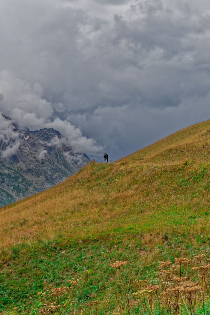 A lone hiker on a grassy hill against dramatic clouds in the French Alps near Marseille.